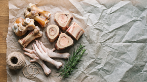 Overhead flat-lay of assorted raw bones for bone broth on butcher paper with twine and rosemary